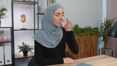 Thirsty Muslim Woman Sitting at Home Holding Glass of Natural Aqua Make Sips Drinking Still Water