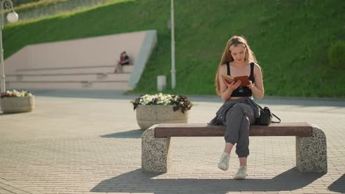Woman Reading Book on Bench in Urban Park