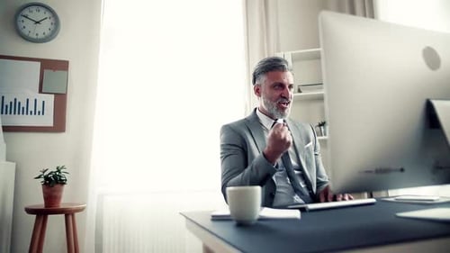 Businessman with Computer Sitting at the Table in an Office, Expressing Excitement