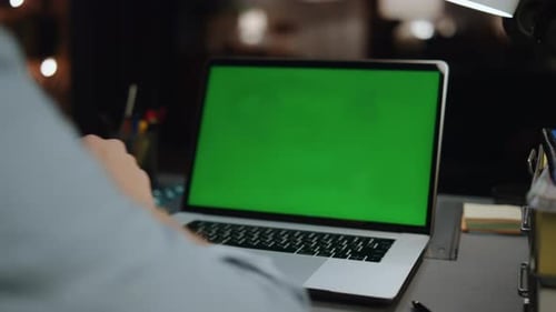 Unrecognizable man watching mockup laptop with green screen at home late at night