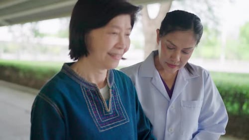 Close-up of the face of an Asian nurse supporting an elderly woman walking outside her home.