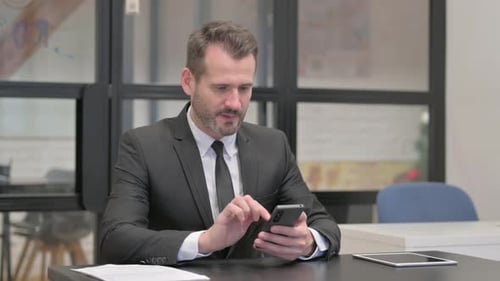 Businessman Cheers While Using Smartphone at Office Desk
