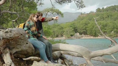 A young loving couple of travelers sitting by the sea on a tree, discussing where to go next.