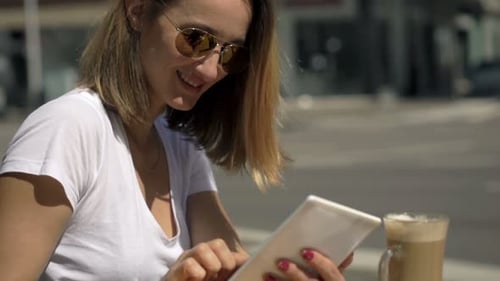 Woman Using Tablet Computer And Drinking Coffee In Cafe In City