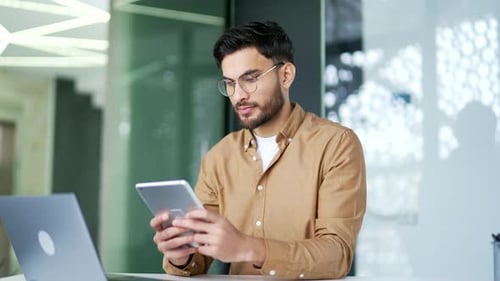 Handsome businessman is using digital tablet while sitting at workplace in business office. Manager