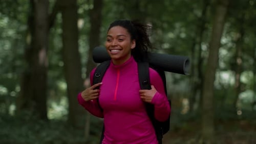 Young Positive African American Woman with Backpack Exploring Woodland Walking in Forest and Smiling