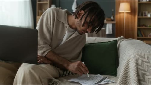 Adult Man Working from Home on Laptop and Paperwork