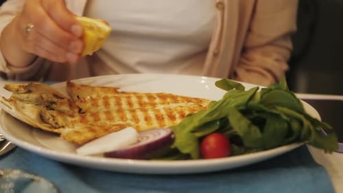 Squeezing Lemon on Grilled Fish and Salad Plate