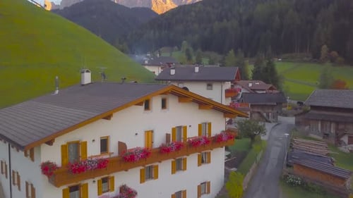 Aerial drone shot rising over a small quaint village with houses beneath the epic mountain peaks of