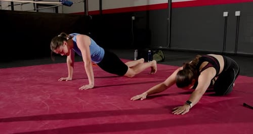 Deux apprenties se déplaçant à travers des pompes et des burpees lors d'un exercice de musculation dirigé par un entraîneur sur un ring de boxe