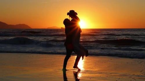 Silhouette of couple during a sunset on beach, where the boyfriend lifts his girlfriend in his arms