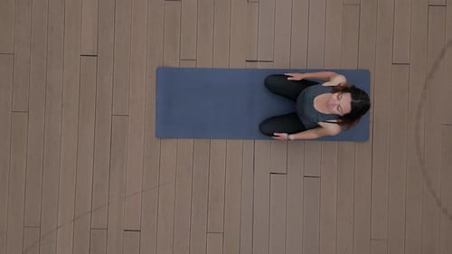 A Young Woman is Doing Yoga on a Mat on a Wooden Floor Topdown View From a Drone