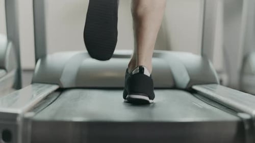 Closeup Athletic Feet Running on Treadmill in Fitness Gym. Back View Of