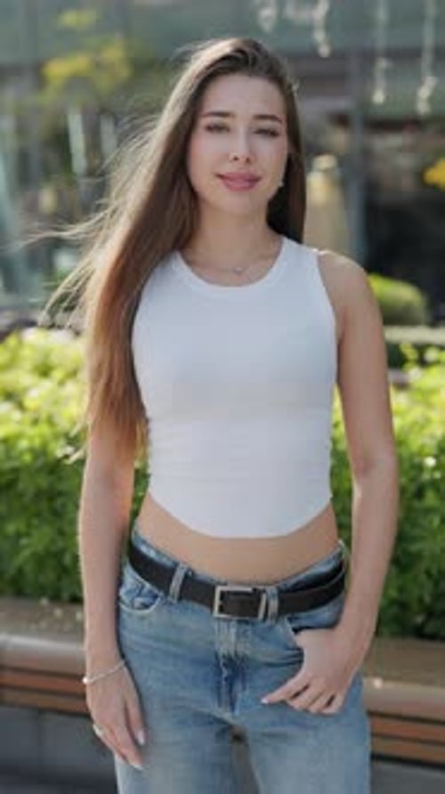 Portrait of Young Woman with Loose Hair in Casual Clothes Smiles in Urban Garden