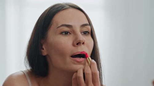 Glamorous young woman applying red lipstick in mirror