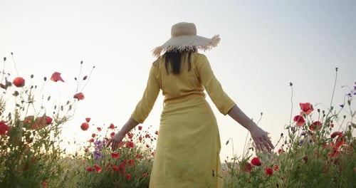 Brunette Woman in a Yellow Dress and Straw Hat Walking in Poppy Field at Sunrise