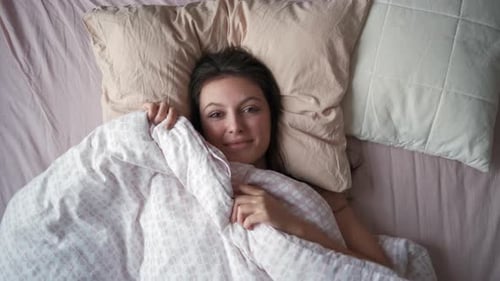Woman Lies in Bed Under Blanket Smiling
