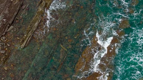 Wellen prallen über die felsige Küste, Wasser spritzt gegen zerklüftete Küstensteine und Meeresrauschen