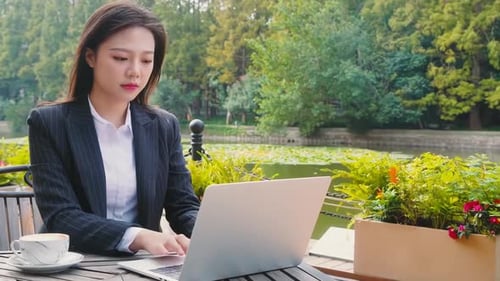 Serious positive businesswoman manager laptop computer work drinking coffee outside office building