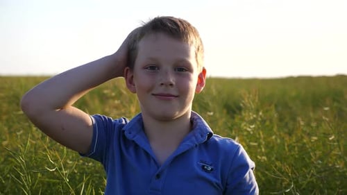 Little Smiling Boy with Freckles Looks Into Camera Against Background of Green Field Portrait of