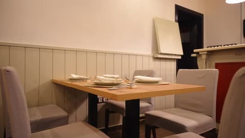 Cozy restaurant with neatly set table and chairs, ready for dining. Pan right