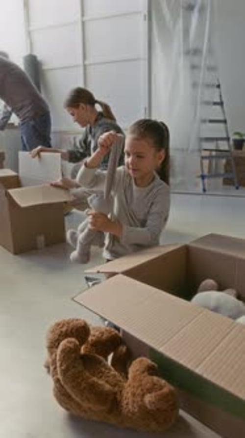Menina colocando brinquedos macios em caixa de papelão contra seus pais