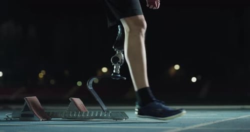 Cinematic shot of young disable man with legs prosthesis prepares to launch off the start line wit