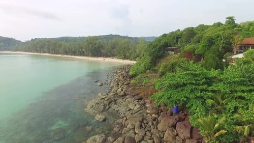 Aerial drone ascending shot of a rocks and beach on a tropical Thai island with resort and clear oce