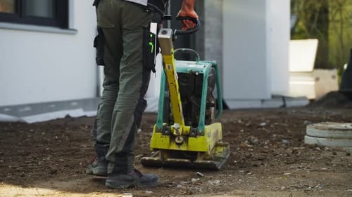 Ouvrier du bâtiment nivelant le sable avec une machine compacteur à plaques vibrantes avant de poser des carreaux.