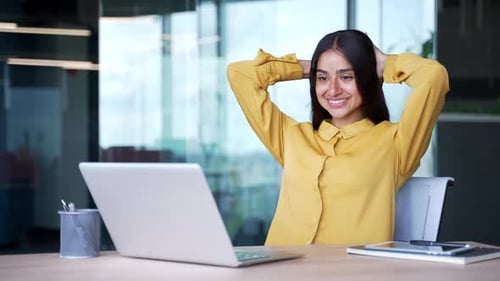 Happy businesswoman sitting at desk in office finished work on laptop. Smiling satisfied female