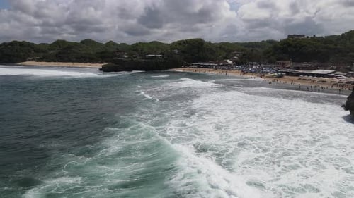 Drohnenaufnahme von Sonnenschirmen, Booten und Menschen, die am Strand in Yogyakarta, Indonesien, Urlaub machen
