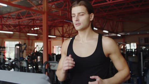 Jovem atleta caucasiano masculino com um corpo musculoso correndo na esteira com um rosto focado