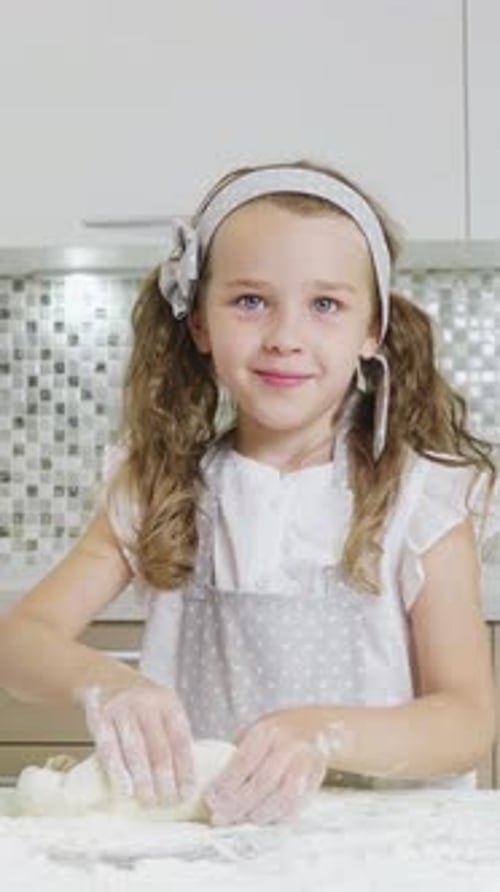 Jeune fille avec des nattes faisant joyeusement cuire dans une cuisine lumineuse de la farine éparpillée sur le comptoir