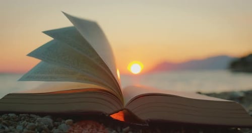 Seiten eines offenen Buches, das während des farbenfrohen Sonnenuntergangs im Sommer in der Meeresbrise blättert