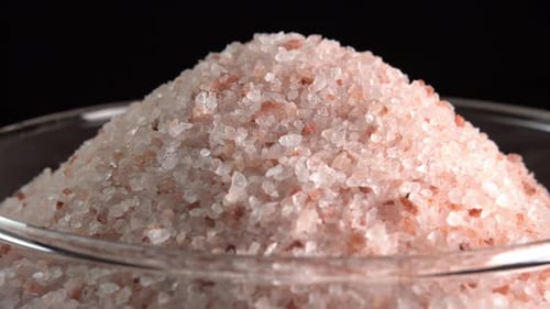 Pink himalayan salt or rock salt rotating in glass bowl side light. Trace minerals salt used