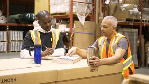 Warehouse teamwork mid adult men discussing shipping plans holding clipboards