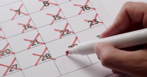 Hand Marking Off Days on Calendar with Red Marker CloseUp View