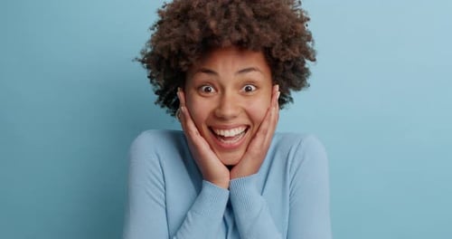 Positive Excited Dark Skinned Woman Clasps Hands with Joy Being in Good