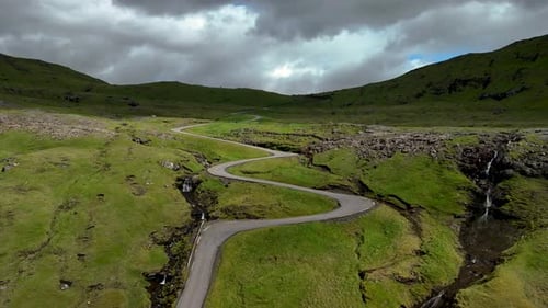 Scenic Winding Road Through Lush Hills in the Faroe Islands Under a Cloudy Sky