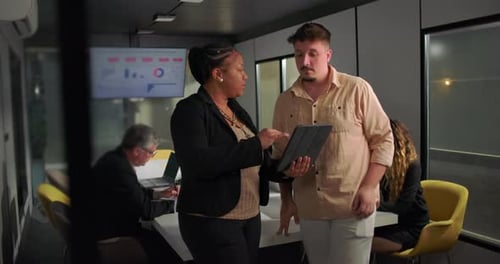 African American businesswoman showing tablet to young male colleague during office meeting,