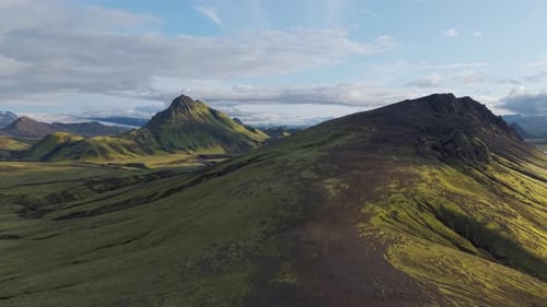 Sharp volcanic peak rises over mossy slopes and valleys