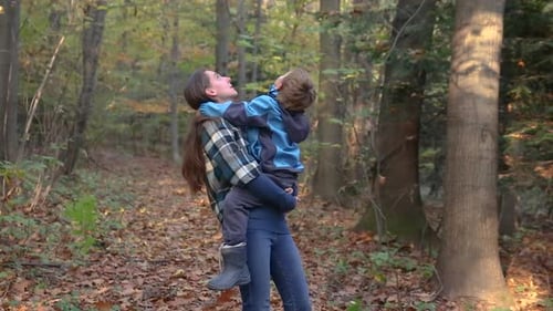 Mother holds son in her arms, explaining the nature in autumn forest
