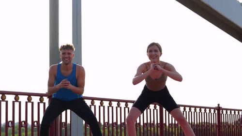 Happy Attractive Fitness Couple Wearing Sportswear and Working Out Outdoors on the Bridge Stretching