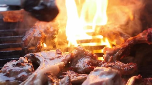 Close-up of flame-grilled being turned meat on the BBQ.