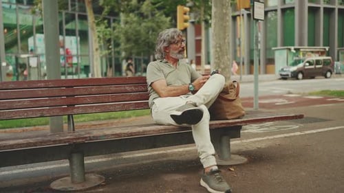 Man Sitting On Bench Using Cellphone In City