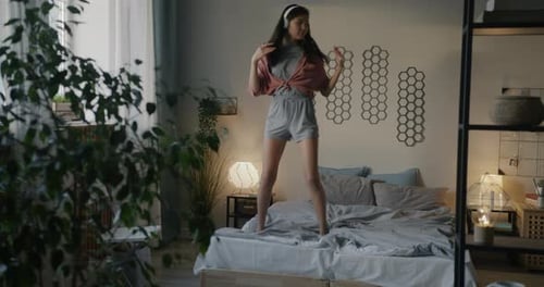 Portrait of Cute Asian Woman Dancing and Singing Having Fun on Bed Listening to Music with