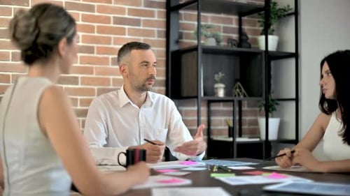 Three people are working and talking in the office. Papers with graphs and information