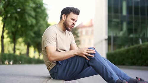 Athlete suffers from leg pain, calf muscle spasm during a workout sitting on sidewalk of a city