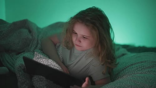 Kind schaut nachts Tablet im Bett zu Kind nutzt Tablet zur Unterhaltung vor dem Schlafengehen Kind konzentriert sich auf