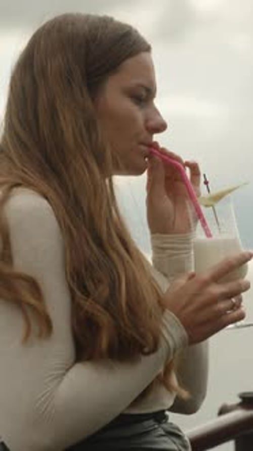 The young woman drinks a cocktail and admires the sea from a high mountain. Vertical video Social Me